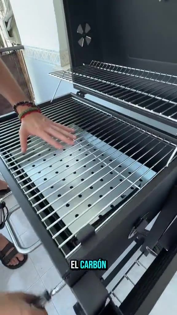 Mano señalando las rejillas cromadas de una parrilla de carbón